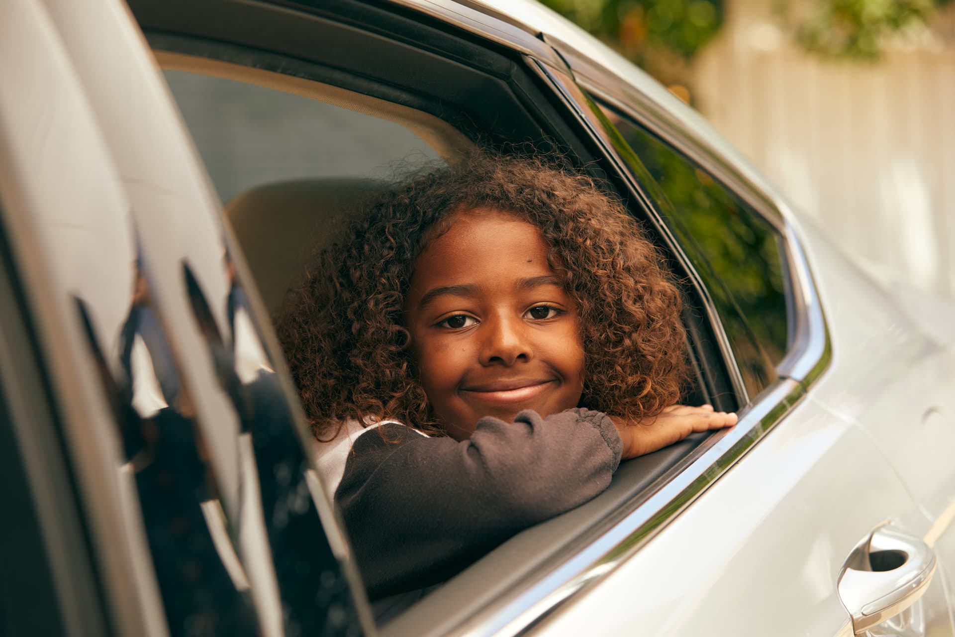 Young child with curly hair smiling warmly while looking out of a car window