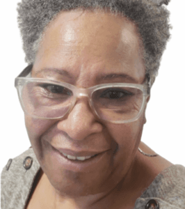 Close-up portrait of a person with silver hair wearing transparent frame glasses, showing a genuine warm smile
