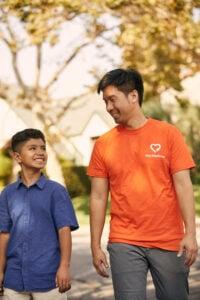 Adult mentor in orange shirt and youth in blue polo sharing a joyful moment outdoors with autumn trees in background