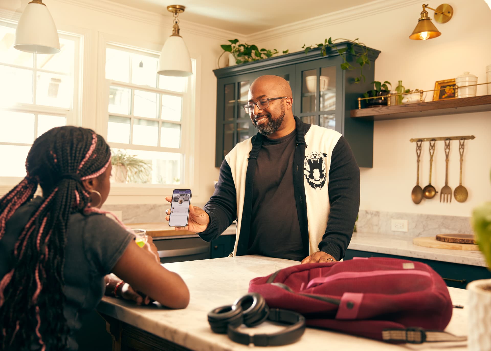 Adult and teenager having a conversation in a modern kitchen while looking at a smartphone, with backpack and headphones on counter