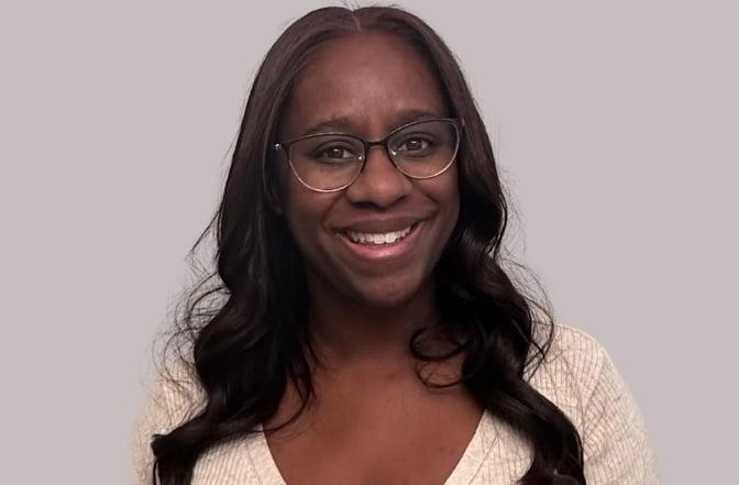 Professional portrait of a woman wearing glasses and a cream sweater, smiling warmly against a neutral background