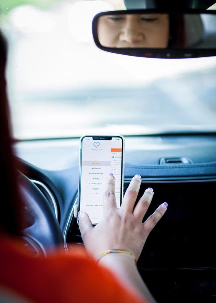 Driver's hand interacting with smartphone mounted on car dashboard, seen through rearview mirror reflection