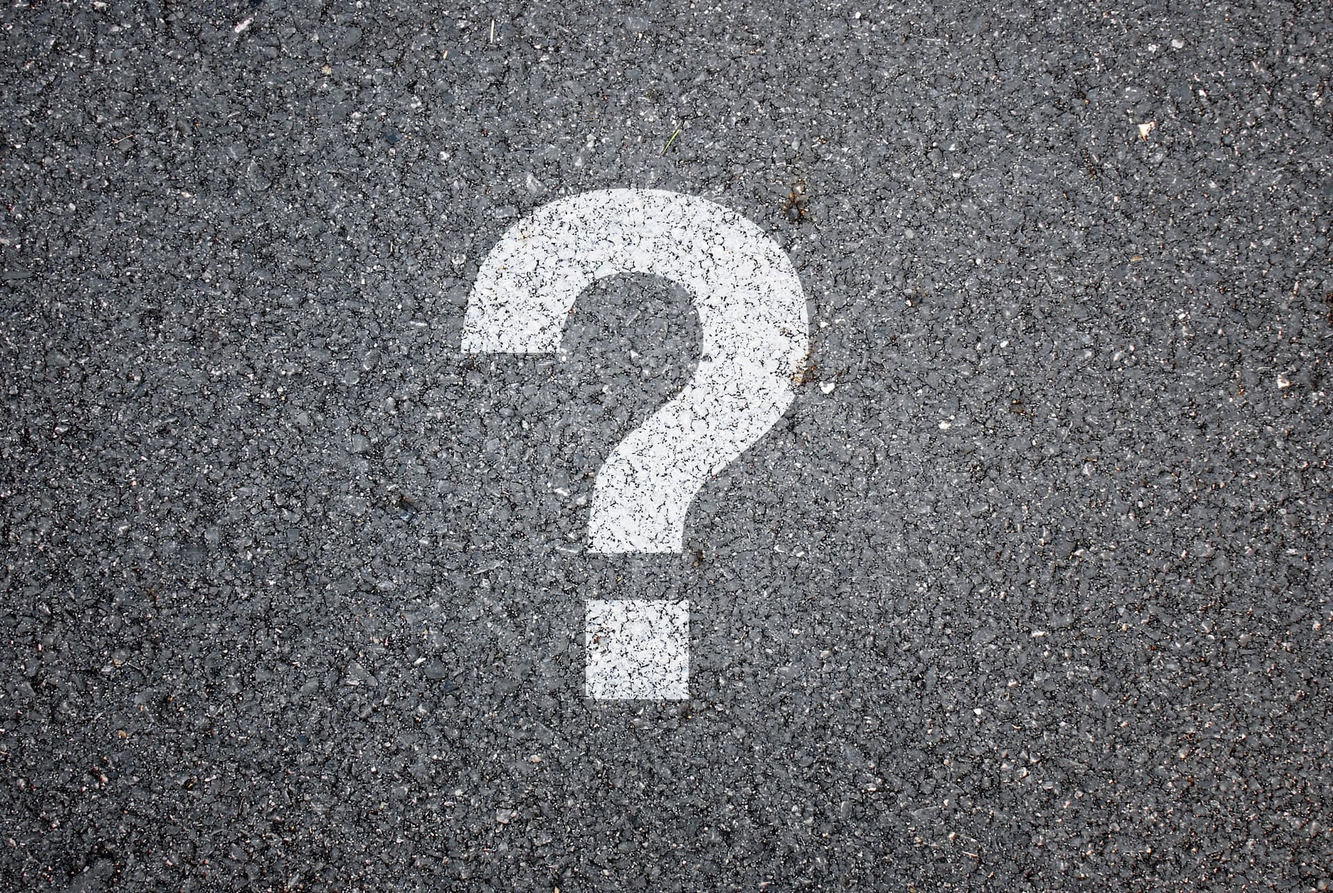 A white painted question mark symbol on dark asphalt pavement
