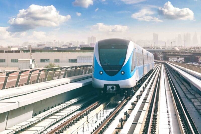 Sleek blue and white metro train on elevated tracks with city skyline in background under partly cloudy sky