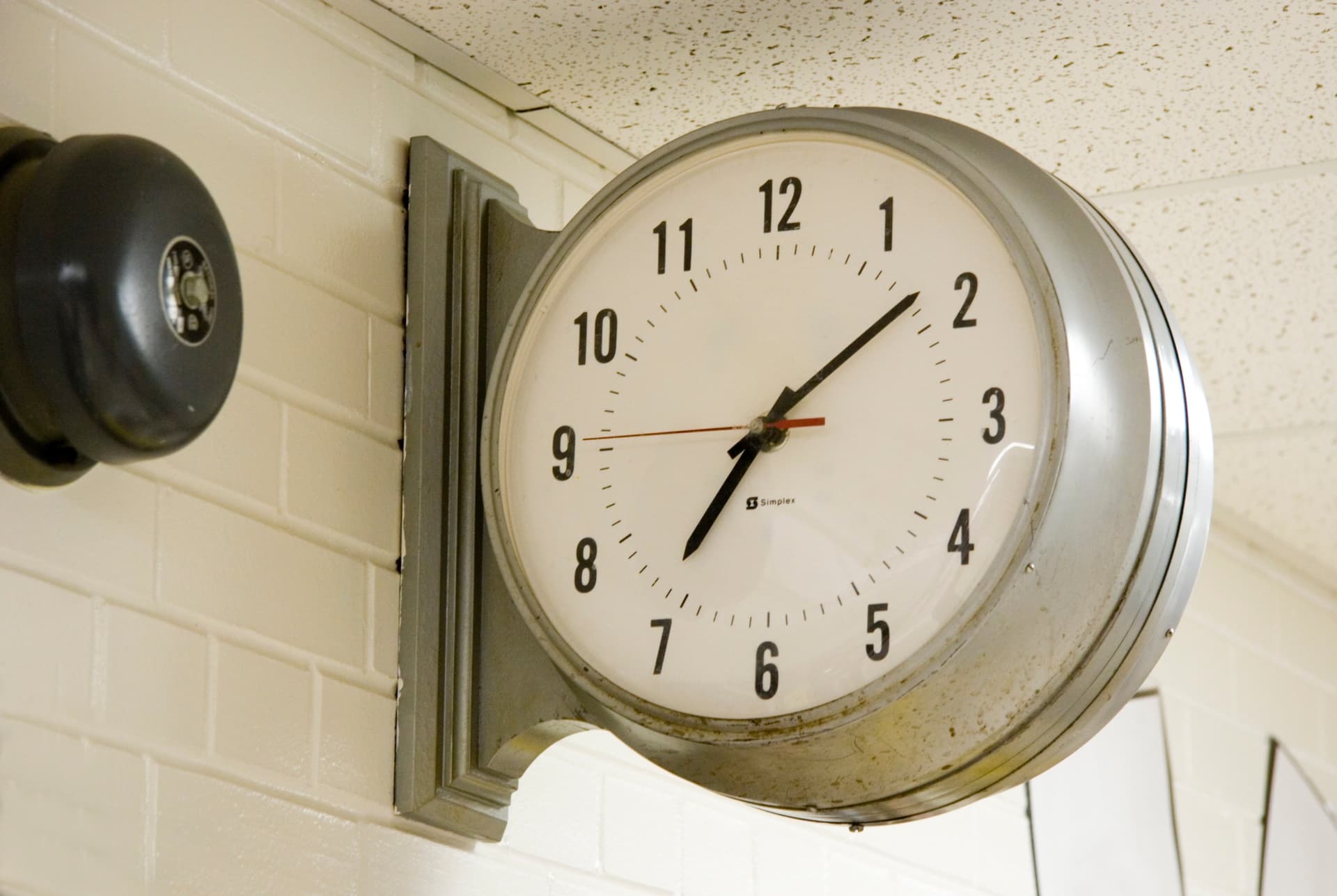 Large round industrial wall clock mounted on white tile wall showing approximately 10:10 time