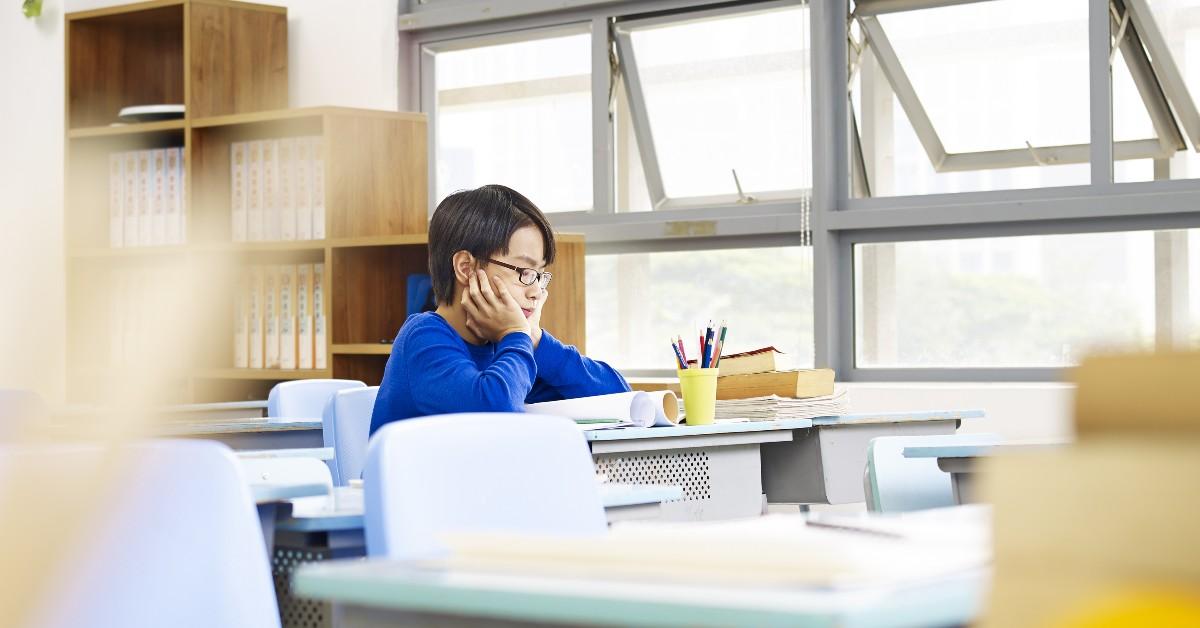 Student in blue sweater sitting at desk in classroom, studying with books and stationery