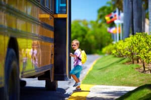 Young student with backpack stepping onto yellow school bus on sunny morning with green landscape in background
