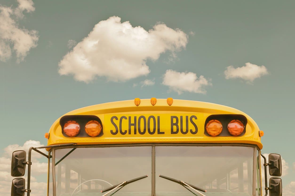 Front view of a yellow school bus with warning lights against a blue sky with white puffy clouds