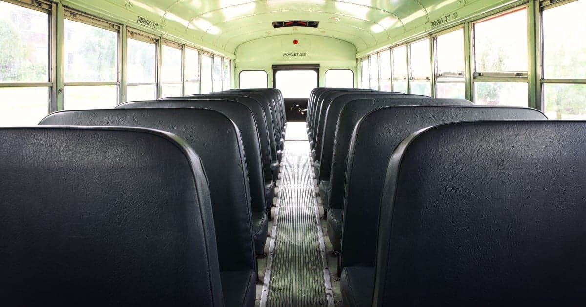 Interior view of an empty school bus showing rows of black vinyl seats and center aisle leading to the emergency exit door