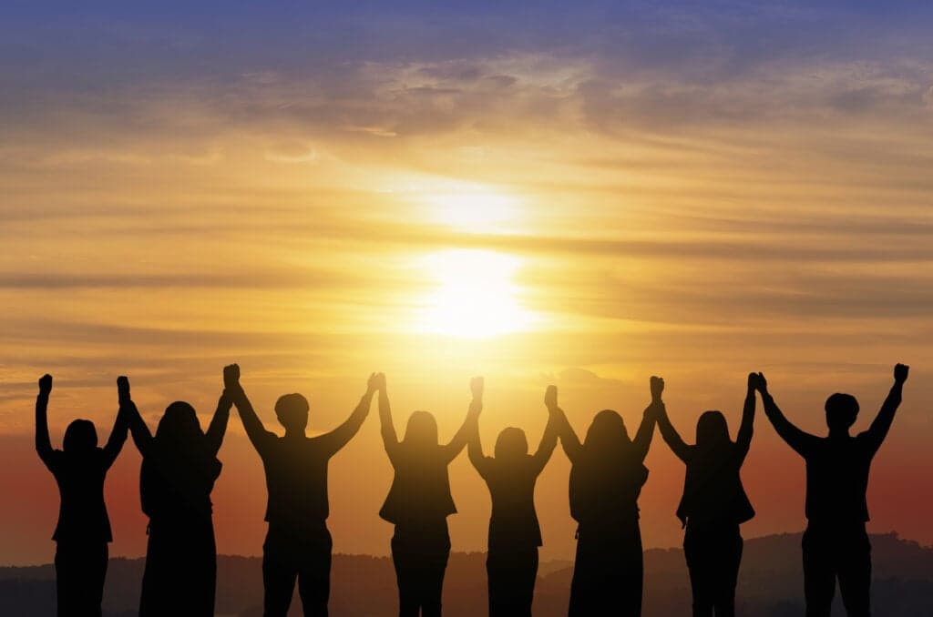 Silhouettes of people holding hands raised in unity against a dramatic golden sunset sky