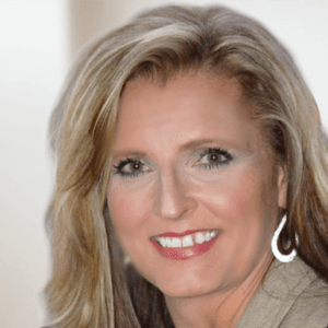 Professional portrait of a woman with blonde hair wearing silver hoop earrings and a warm smile against a soft focus background