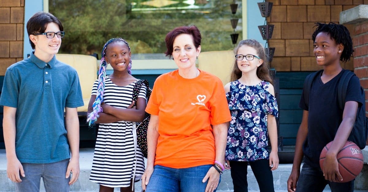 Group of diverse young people with adult mentor in orange shirt standing together outside brick building, one holding basketball