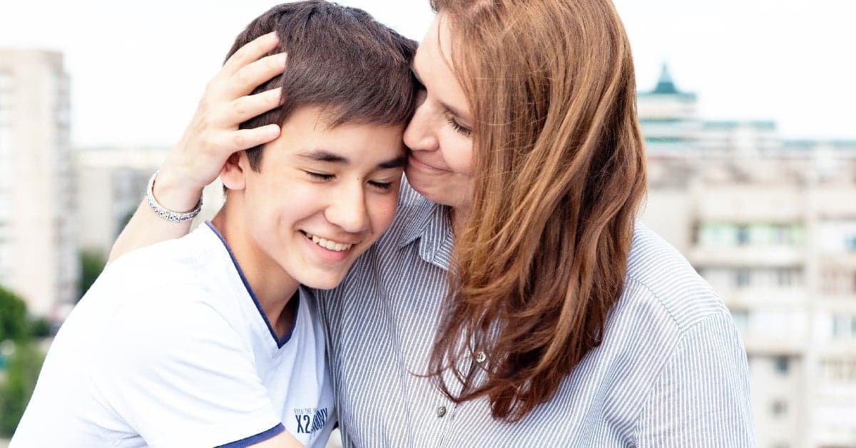 Mother and teenage son sharing an intimate moment, mother gently touching son's head as both smile with eyes closed
