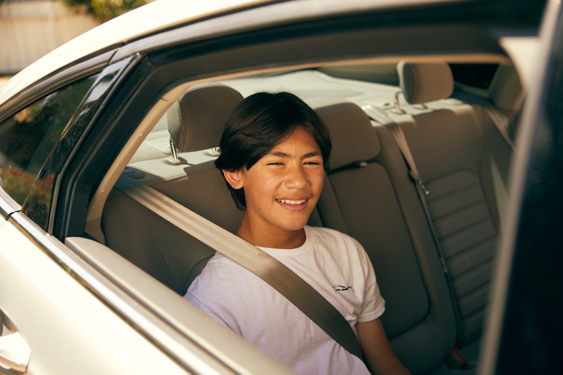 Young teen wearing white t-shirt smiling while sitting in car backseat with seatbelt on