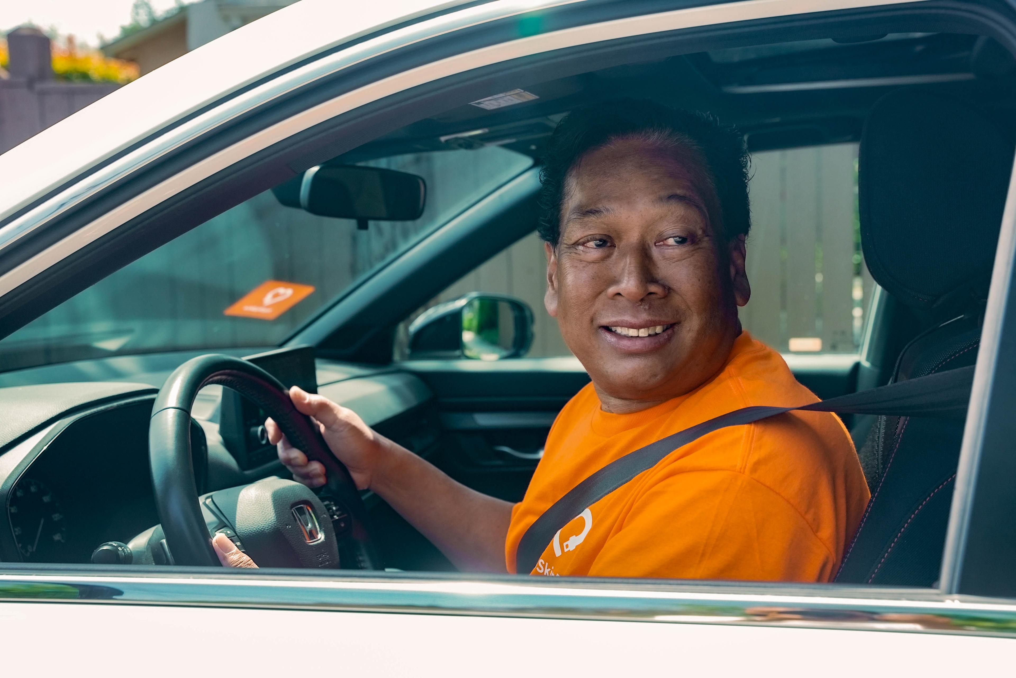 A HopSkipDrive CareDriver smiles from the front seat of his sedan.