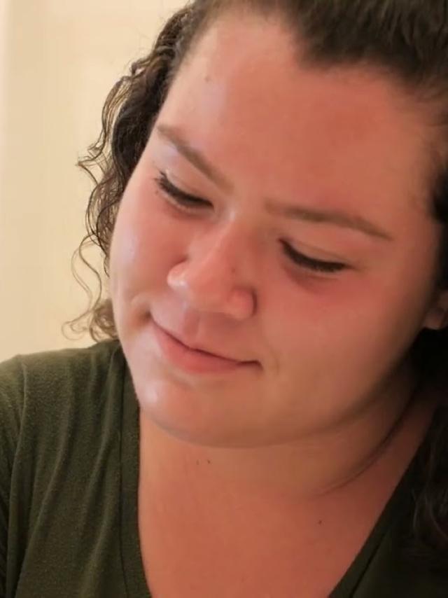 A close-up portrait showing a gentle smile and downward gaze, wearing a green sweater