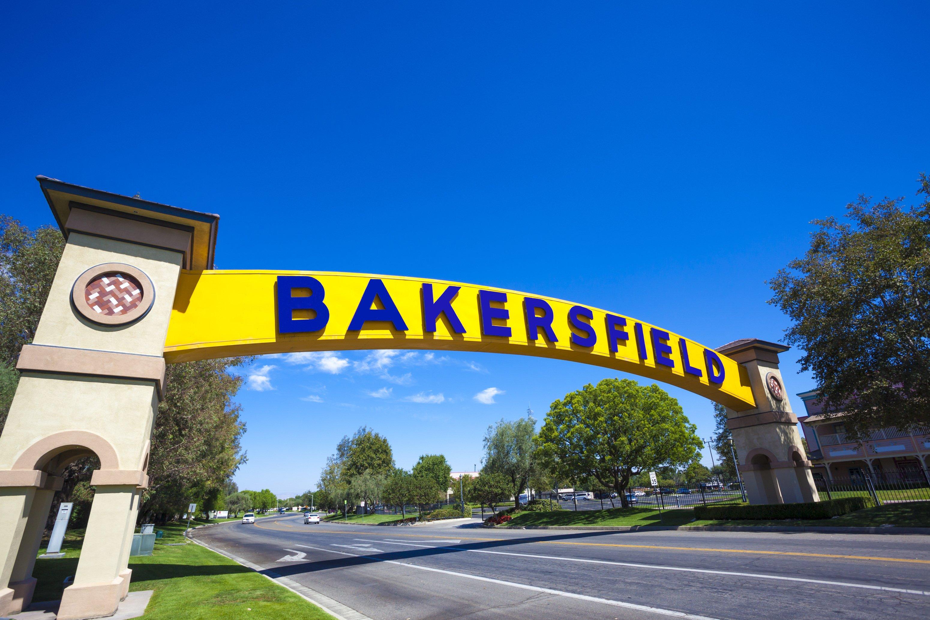Yellow and blue Bakersfield entrance arch spanning across a street with stone pillars and landscaping on a sunny day
