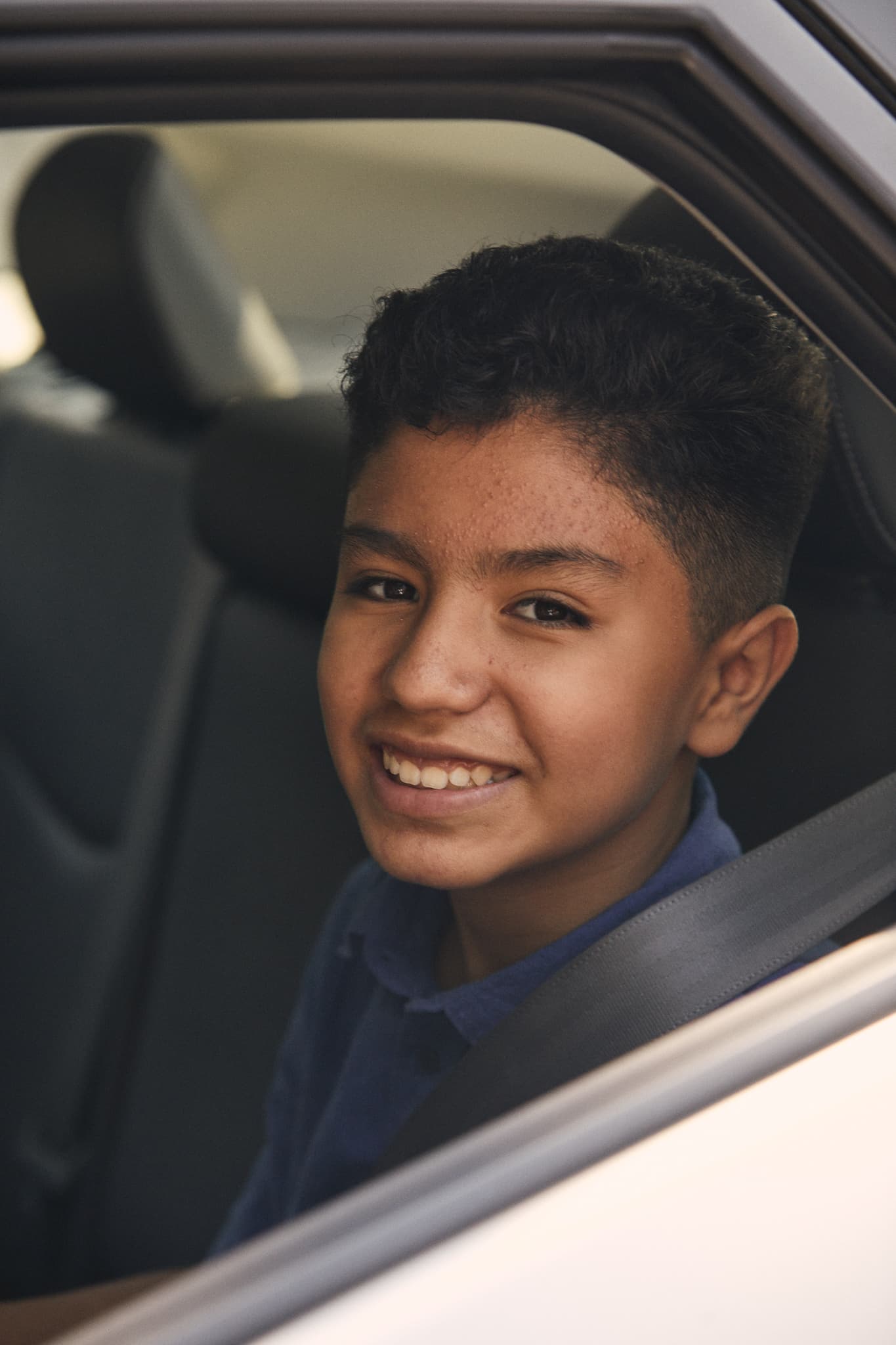Teenage boy with bright smile sitting in driver's seat of car wearing blue shirt