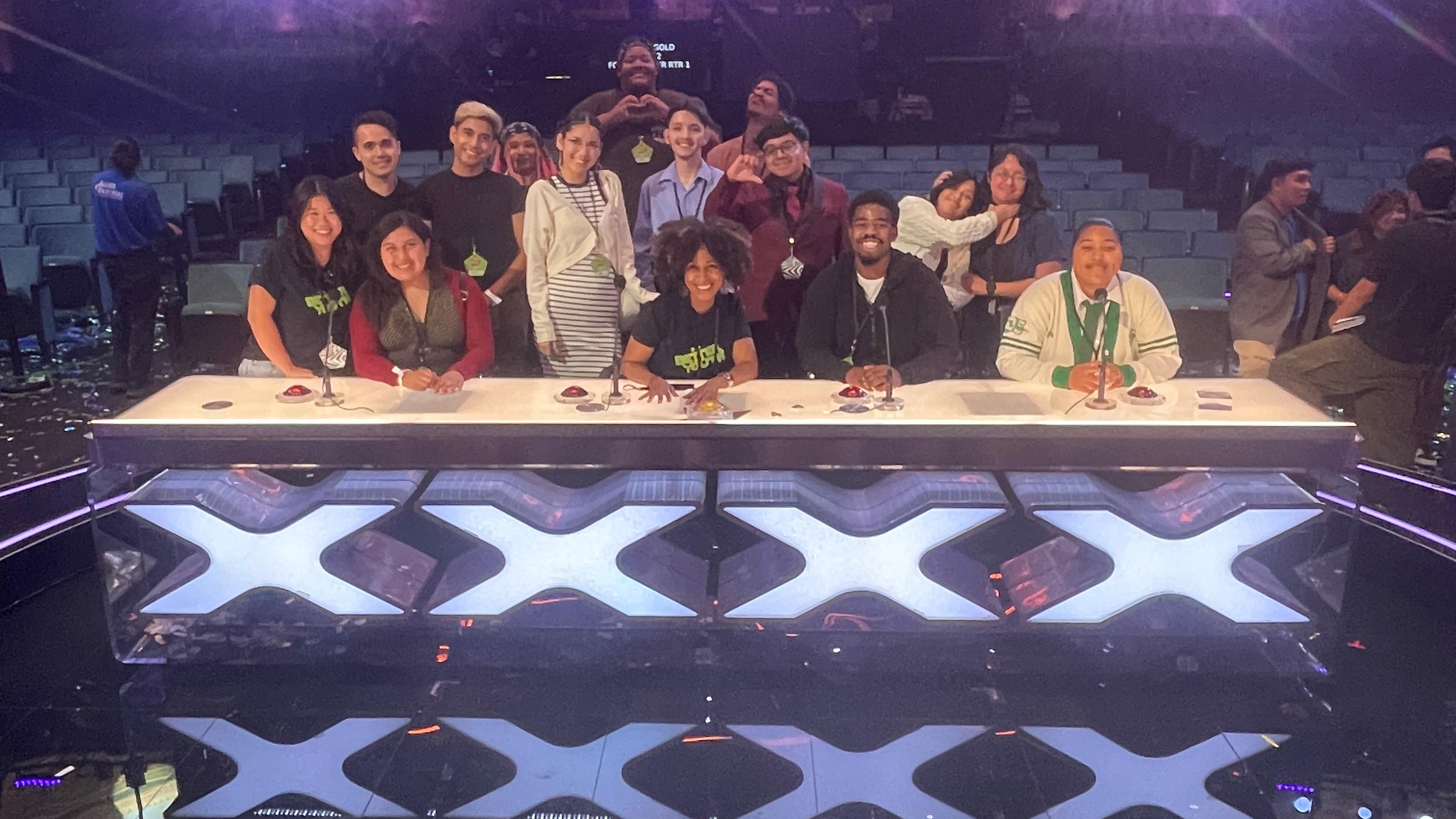 Group photo at the Americas Got Talent judges table with crew members and staff posing together in an empty auditorium