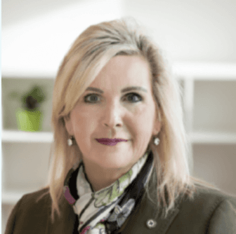 Professional headshot of a woman with blonde hair wearing a dark jacket and patterned scarf, photographed against a light interior background