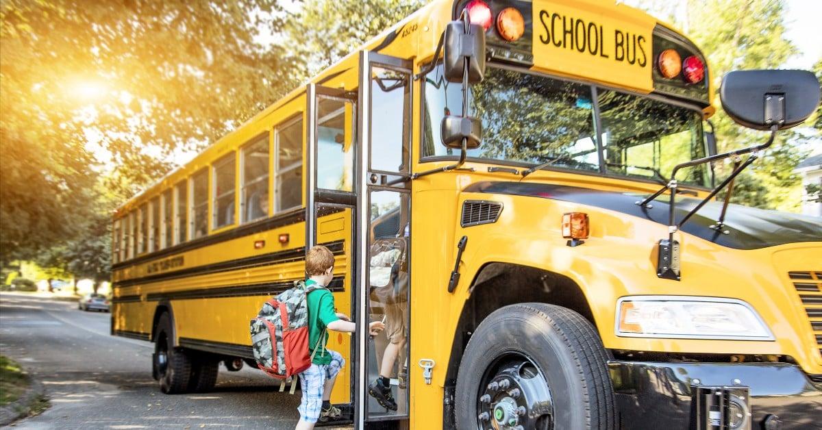 Young student with backpack climbing steps to enter a yellow school bus on a sunny morning