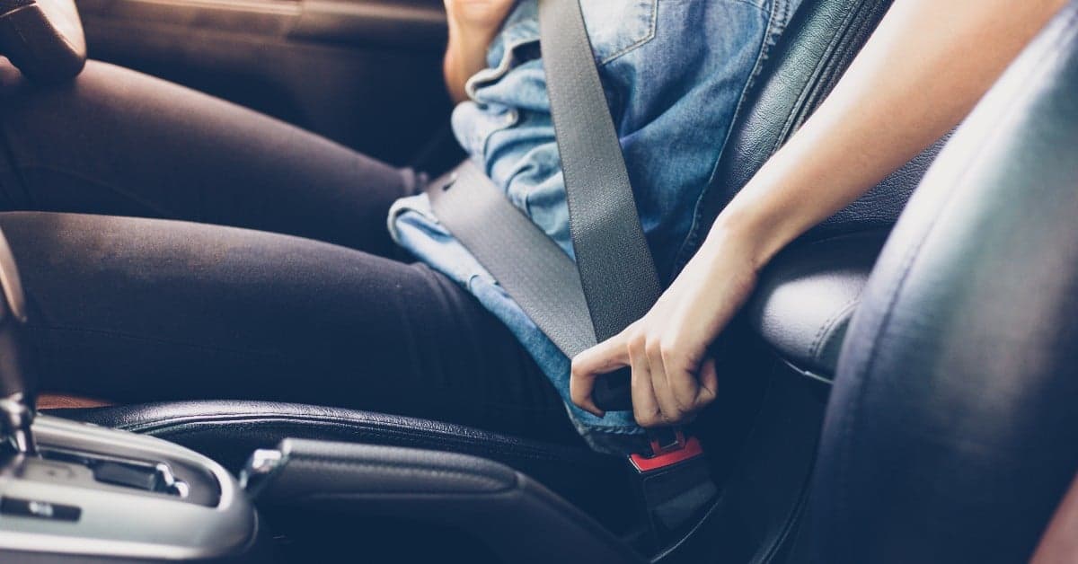 Person buckling a grey seatbelt while sitting in a car with leather seats