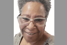 Close-up portrait of a person wearing silver-framed glasses, with short gray hair and a warm, genuine smile