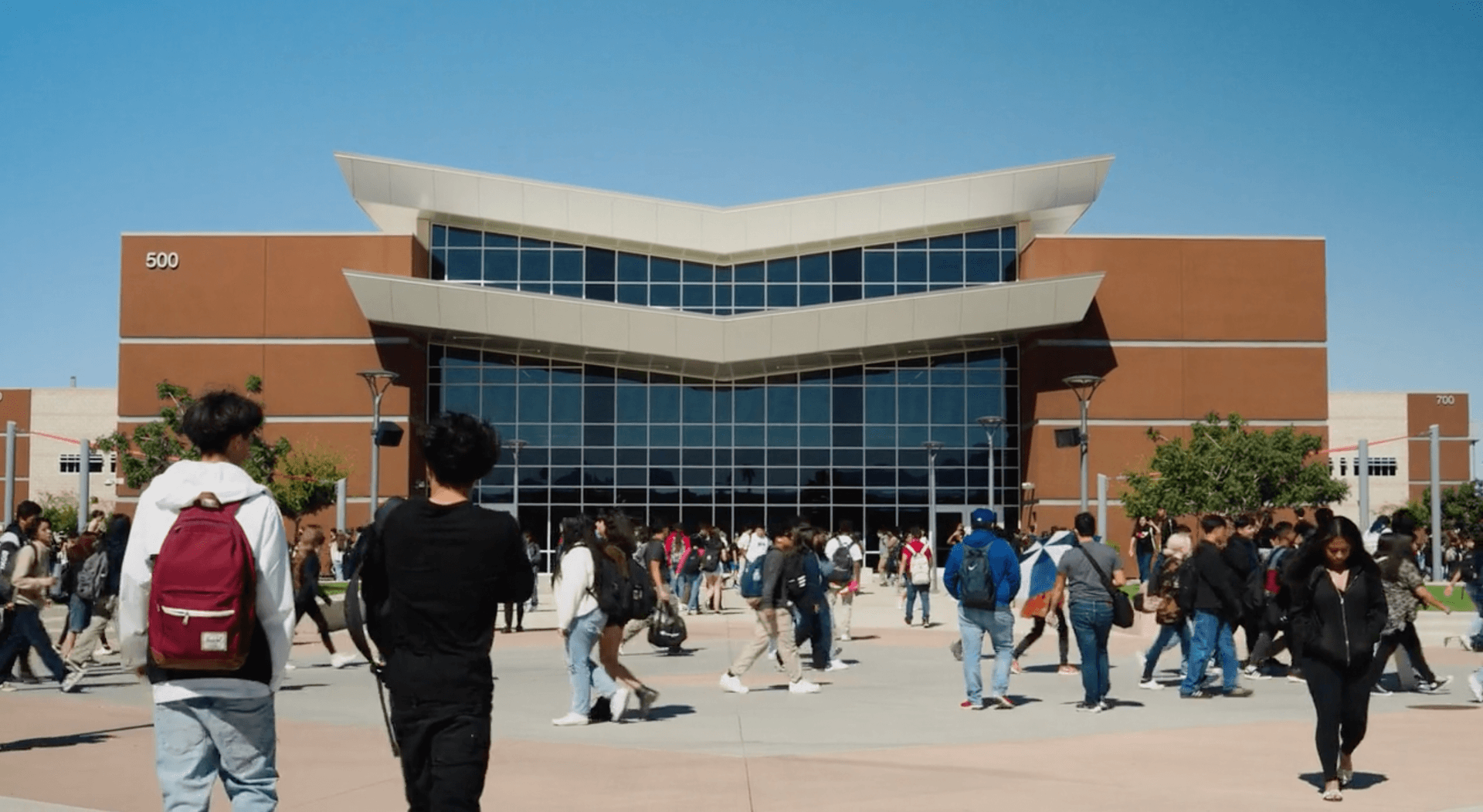 Modern brown and white school building entrance with students gathering outside during break or passing period