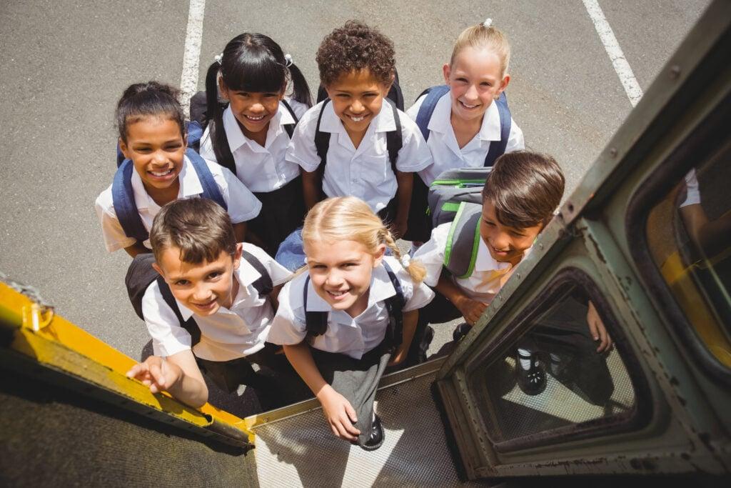 Overhead view of smiling students in school uniforms boarding a yellow school bus, seen from the bus entrance
