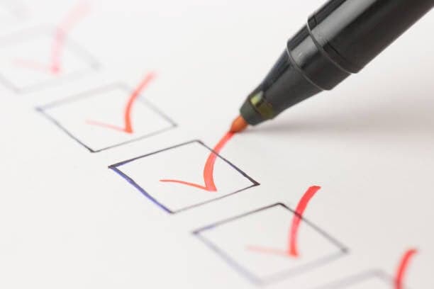 Red marker making checkmarks on a paper checklist with blue checkbox outlines