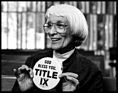Black and white photo of a person holding a circular button displaying 'Title IX' with a joyful expression
