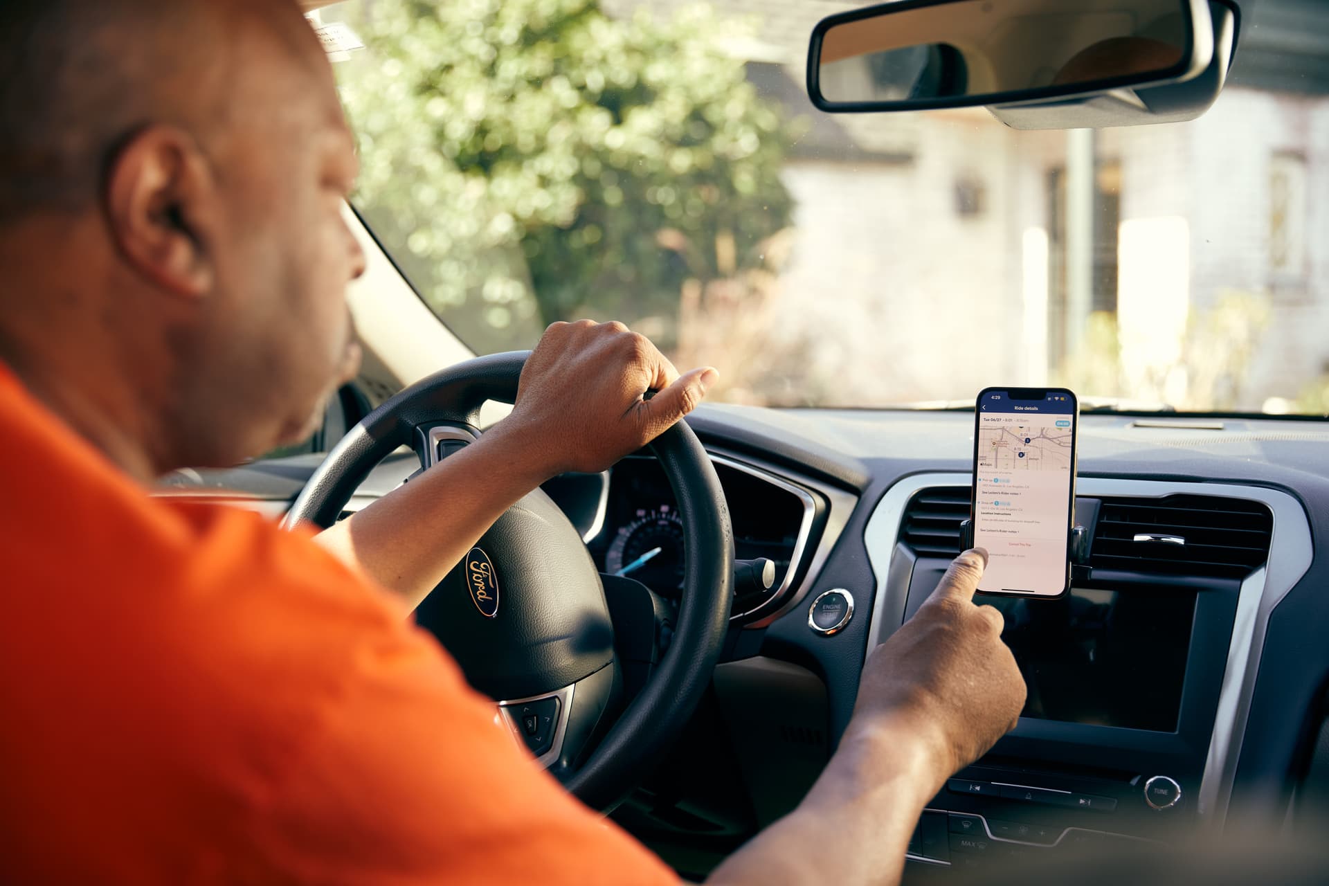 Driver in orange shirt checking navigation app on smartphone mounted in Ford vehicle while driving