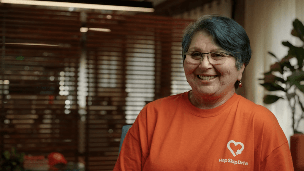 Woman wearing orange HopSkipDrive t-shirt smiling warmly at camera in office setting