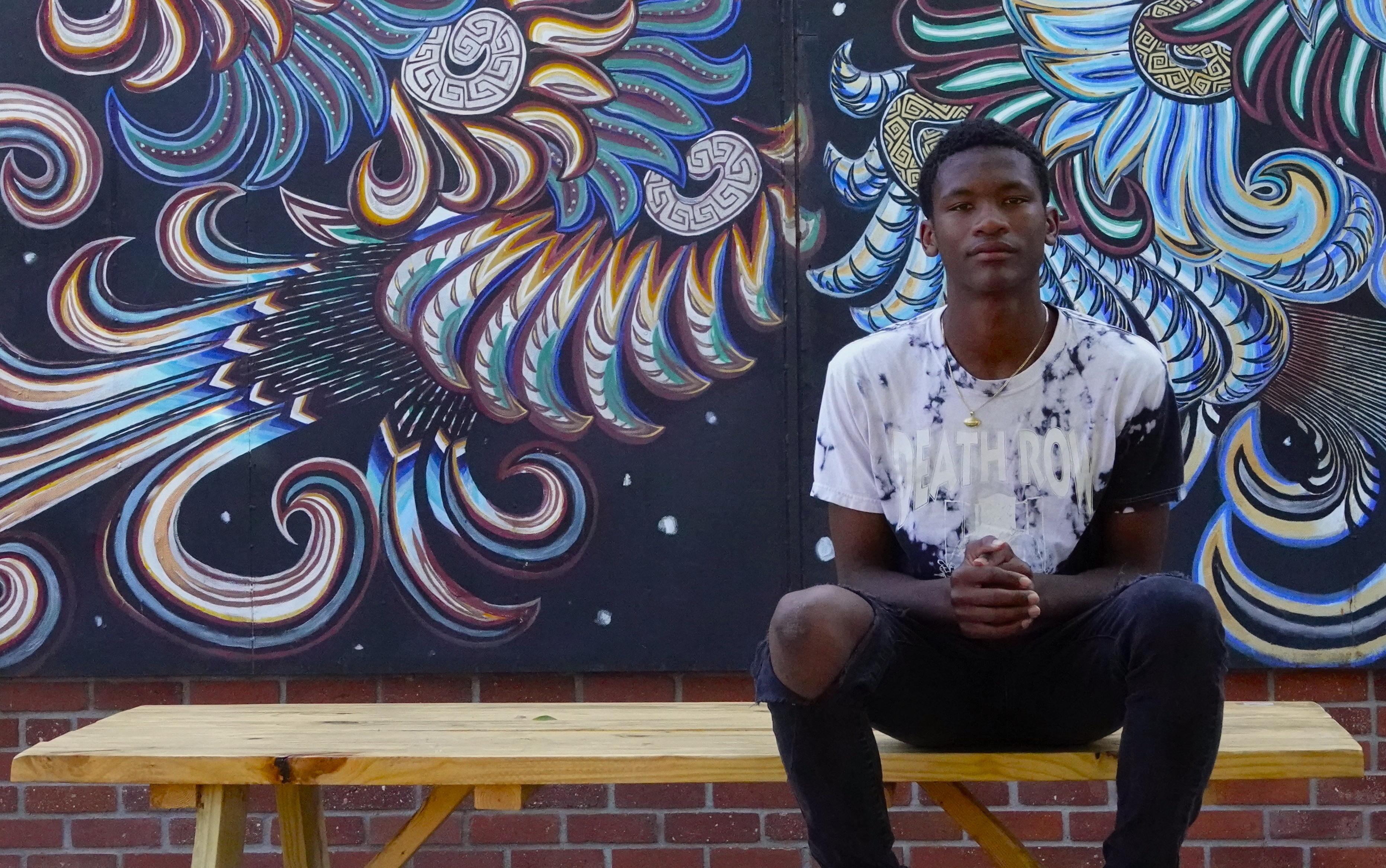 Person sitting on wooden bench against colorful swirling street art mural featuring blue and orange patterns